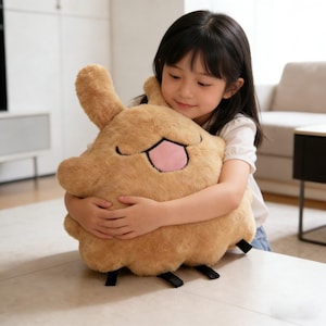 May include: A plush, brown stuffed animal with a smiling face and a pink tongue is being hugged. The toy has a fluffy texture and black feet. The toy is a soft, cuddly item.