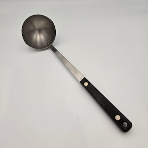 May include: A stainless steel ladle with a black handle. The ladle has a round bowl and a long, thin handle. The handle is black with two silver rivets. The ladle is designed for serving soups, stews, and sauces.