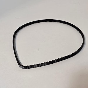 May include: A black timing belt with a toothed design. The belt has text printed on it, including "NITTA" and "471-3GT". The belt is circular and appears to be new.
