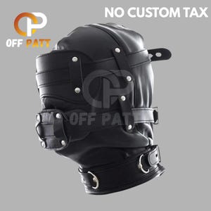 Puede incluir: Capucha de cuero negro con múltiples correas y herrajes metálicos. La capucha tiene una parte superior redondeada y una correa para la barbilla con un anillo metálico. El texto "NO CUSTOM TAX" es visible en la parte superior.