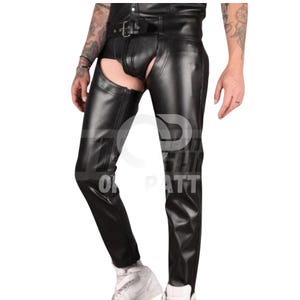 May include: Black leather chaps featuring a high-waisted belt with a metal buckle, a front codpiece design, and open-thigh construction. The garment has a smooth, polished finish and extends down to the ankles, showcasing a fitted, structured silhouette.