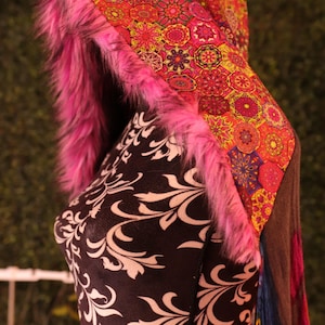 Puede incluir: Una prenda con capucha con un diseño vibrante y estampado en tonos rojos, naranjas y amarillos. La capucha está adornada con piel sintética rosa brillante. La prenda se exhibe en un maniquí con un estampado floral en blanco y negro.