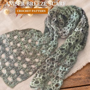 May include: A crochet scarf featuring an openwork pattern in variegated shades of green, brown, and grey. The text "The AMBER BREEZE SCARF CROCHET PATTERN" is displayed at the top, accompanied by dried floral elements in the background.