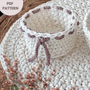 May include: A handmade, off-white crochet basket with a drawstring closure and a matching placemat. The basket is trimmed with a mauve-colored yarn. The text "PDF PATTERN" is in the upper left corner.