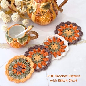 May include: Four handmade crochet coasters in shades of orange, green, and brown, arranged near a decorative teapot and cup. The coasters feature a floral design with scalloped edges. Text on the image reads "PDF Crochet Pattern with Stitch Chart."