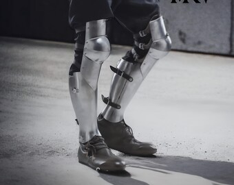 May include: Silver metal leg armor, including knee and shin protection, secured with leather straps. The armor is worn over dark pants and paired with brown leather shoes. The image includes the letters "MNW" in the upper right corner.