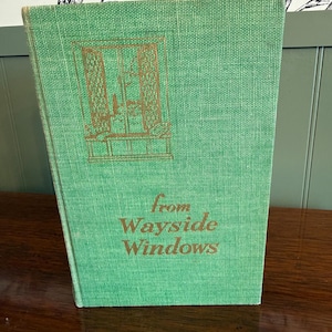 Könnte beinhalten: Ein Vintage-Buch mit dem Titel "From Wayside Windows" mit grünem Einband. Das Cover zeigt eine goldene Illustration eines Fensters und goldene Schrift. Das Buch hat ein strukturiertes Aussehen und ist leicht angewinkelt.