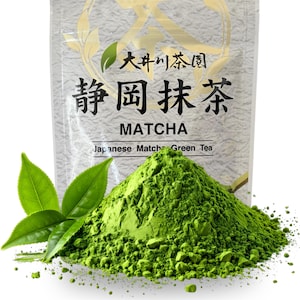 May include: A vibrant green pile of matcha powder sits in front of a package with Japanese text and the word "MATCHA". Fresh green tea leaves are placed near the powder. The package reads "Japanese Matcha Green Tea".