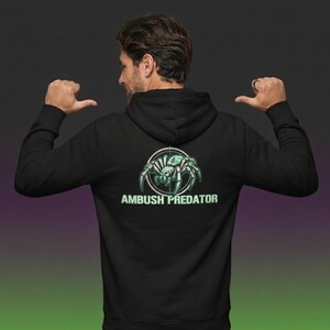 May include: Black hooded sweatshirt with a graphic of a spider inside a target reticle, with the words "AMBUSH PREDATOR" below. The spider and text are in a teal color. The person is wearing the sweatshirt and is facing away from the camera.
