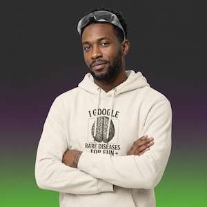 May include: A beige hoodie with the text "I GOOGLE RARE DISEASES FOR FUN+" and a brain graphic. The person in the image is wearing safety glasses on their head.