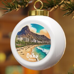 May include: White Christmas ornament with a gold cap and hanger. The ornament features a colorful illustration of a beach scene with the text "Oahu Hawaii". The illustration includes a mountain, buildings, and ocean.