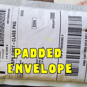 May include: A white padded envelope with black text and a barcode. The text "PADDED ENVELOPE" is written in large yellow letters. The envelope is labeled "USPS FIRST-CLASS PKG".