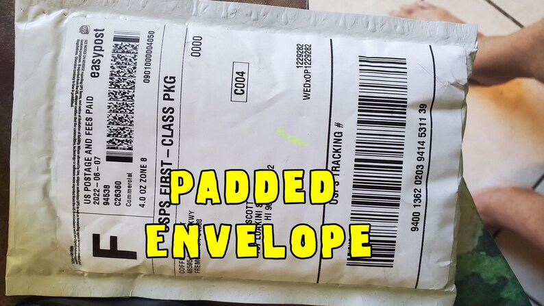May include: A white padded envelope with black text and a barcode. The text "PADDED ENVELOPE" is written in large yellow letters. The envelope is labeled "USPS FIRST-CLASS PKG".