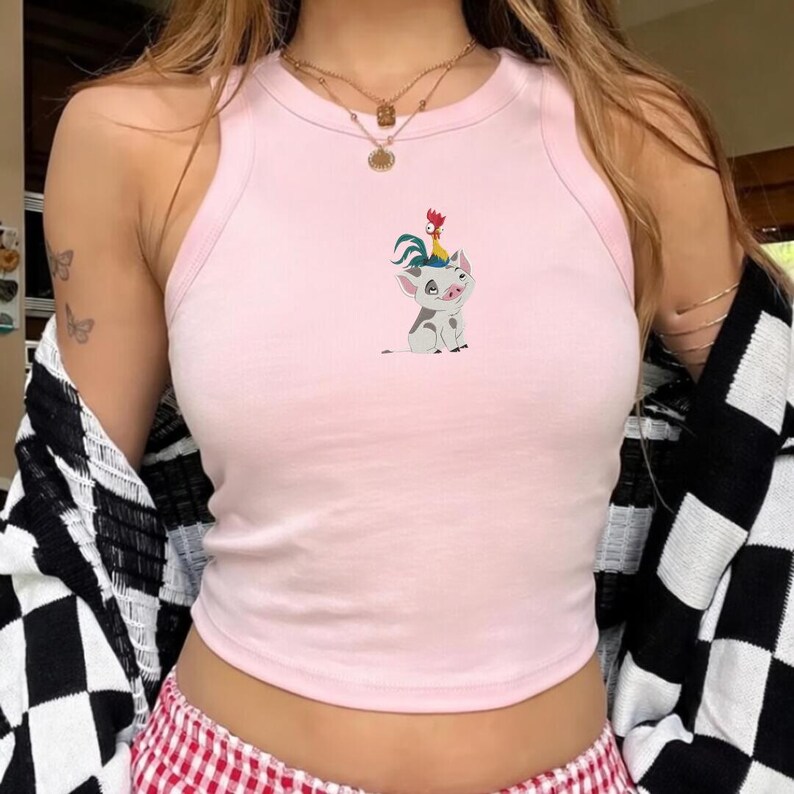 May include: A light pink crop top with a round neckline and a cartoon graphic of a pig and rooster. The top is sleeveless and made of a soft material. The pig is white with gray spots and the rooster is red and yellow.