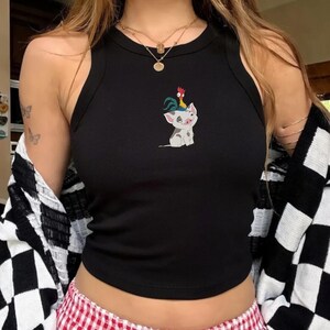 May include: Black ribbed tank top featuring a cartoon pig with a rooster on its head. The pig is white with gray spots and a blue tattoo. The rooster is red, yellow, and green. The tank top is sleeveless and has a round neckline.