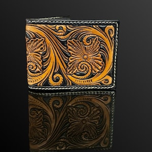 May include: A bi-fold leather wallet featuring intricate hand-tooled floral and scroll patterns. The design showcases a natural tan finish on the raised floral motifs contrasted against a deep black background, finished with white stitching.