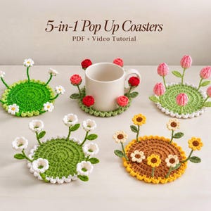 May include: Five circular crochet coasters featuring 3D floral designs including daisies, tulips, and sunflowers. The text 5-in-1 Pop Up Coasters PDF + Video Tutorial is displayed above the items. Each coaster has a green or brown base.