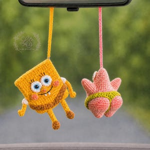 May include: Two hanging crochet ornaments suspended by strings. One is a yellow rectangular character with blue eyes and a brown base. The other is a pink starfish character wearing green trunks. Both are crafted with yarn and feature detailed stitching.