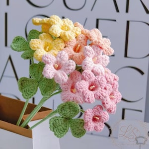 May include: A bouquet of handmade crochet flowers in shades of yellow, peach, and pink, with green leaves and stems. The flowers are arranged in a white paper bag. The background features the word "YOU" in large black letters.