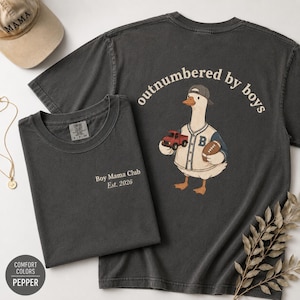 May include: Two charcoal gray t-shirts with white text and a baseball cap. One shirt says "Boy Mama Club Est. 2026". The other shirt has a goose wearing a baseball uniform and the text "outnumbered by boys".