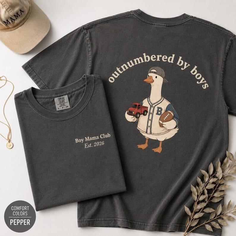 May include: Two charcoal gray t-shirts with white text and a baseball cap. One shirt says "Boy Mama Club Est. 2026". The other shirt has a goose wearing a baseball uniform and the text "outnumbered by boys".