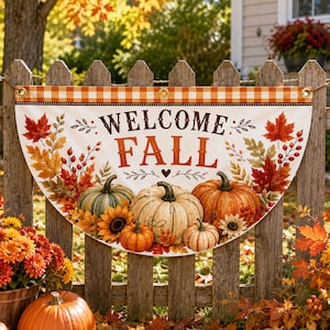 以下が含まれることがあります： WELCOME FALLという文字がダークブラウンとオレンジで書かれた半円形の布製バナー。カボチャ、ヒマワリ、秋の葉のイラストがオレンジ、黄色、緑の色合いで描かれており、チェック柄の縁取りが施されています。