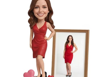 May include: A bobblehead figurine of a woman in a red dress and a gold crown. The figurine is standing next to a framed photo of the same woman. The base of the figurine has the text "Valentine's 2026" and pink heart shapes.