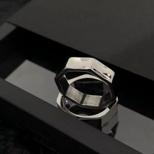 May include: Two silver rings with a geometric design are stacked. The rings have a shiny, reflective surface and are set against a black background. The rings appear to be made of metal. The rings are likely to be worn as jewellery.