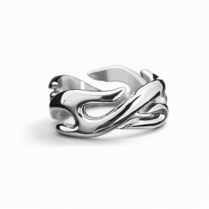 Puede incluir: Anillo plateado con un diseño fluido en forma de llama. El anillo tiene un acabado liso y pulido y una forma abstracta única. El diseño parece envolver el dedo, creando un accesorio llamativo.