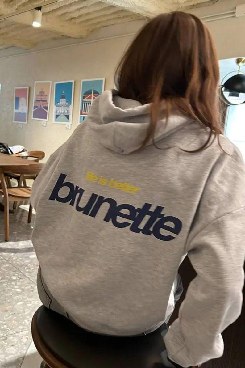 Puede incluir: Sudadera con capucha gris claro con la palabra "brunette" en letras may&uacute;sculas azul marino y las palabras "life is better" en amarillo encima. La sudadera tiene capucha y mangas largas.