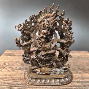Peut inclure: Statue en bronze d'une divinité à plusieurs bras avec une expression féroce. La figure est ornée d'une couronne de crânes et entourée d'un halo de flammes. La statue est détaillée avec des sculptures complexes et repose sur une base décorative.