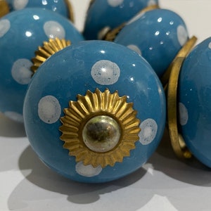 May include: A set of blue ceramic cabinet knobs with white polka dots and gold accents. Each knob is round and has a decorative gold ring around the centre.