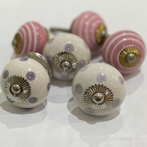 May include: Set of six ceramic cabinet knobs with a white base and purple polka dots. Two knobs have a pink base with white stripes. Each knob has a silver metal accent.
