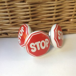 May include: Three red and white ceramic cabinet knobs shaped like stop signs with the word "STOP" in white letters.