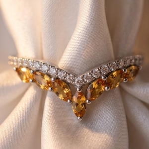 May include: A V-shaped ring featuring a row of marquise-cut yellow citrine gemstones set in silver-toned metal, topped with a delicate band of small, clear round-cut stones that follow the chevron contour of the primary yellow gems.