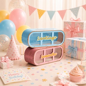 May include: Two stacked rectangular wooden money boxes with rounded edges, one light blue and one pink. Each box features a clear front panel, a slot on top, and the names Santiago and Samantha in yellow script. The words give, save, and spend are printed below.