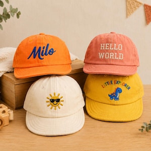 May include: Four baseball caps in orange, coral, cream, and yellow. The orange cap features the blue embroidered name Milo. The coral cap has white embroidered text reading Hello World. The cream cap shows a sun icon, and the yellow cap displays a blue dinosaur with the text Little Explorer.