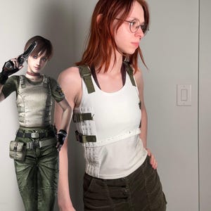 May include: A person wearing a white tank top with olive green straps and a matching skirt. The top has a white panel with olive green straps and buckles. The person is wearing round glasses and has red hair.