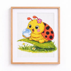 Pode incluir: Imagem emoldurada de ponto cruz representando uma joaninha de desenho animado. A joaninha amarela tem asas vermelhas com bolinhas pretas e uma flor rosa. Ela segura um globo azul e está sentada em uma folha verde, com grama e flores.