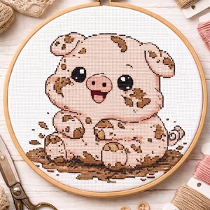 May include: Cross-stitch embroidery of a piglet covered in mud, set in a wooden hoop. The piglet is pink with brown spots and a happy expression. The craft supplies include thread, scissors, and wooden buttons.