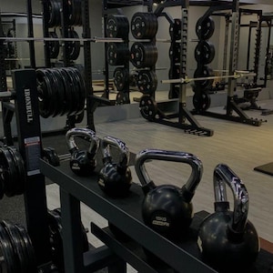 Könnte beinhalten: Ein Fitnessstudio-Interieur mit Gewichthebeausrüstung. Schwarze Kettlebells, einige mit der Aufschrift "10KG", stehen auf einem Rack. Gewichtsplatten und Langhanteln sind auf Racks und Ständern sichtbar. Das Wort "IRONBULL" ist aufgedruckt.