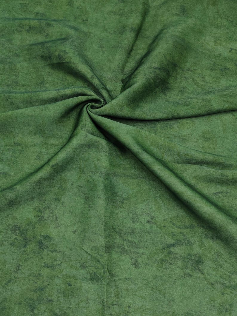 May include: Close-up of green fabric with a mottled texture. The fabric has a swirling pattern with darker green accents, creating depth. The material appears soft and pliable, suitable for textile projects. The overall effect is of a rich, textured textile.