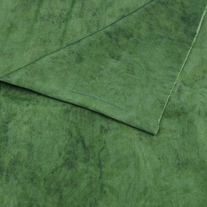 May include: Close-up of green fabric with a marbled effect. The material has a folded corner, showing a lighter green shade. The fabric appears soft and flowing, potentially for clothing or home furnishings. The texture is detailed.