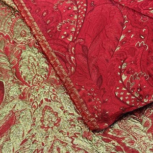 Peut inclure: Gros plan sur deux tissus aux motifs cachemire ornés. L'un est rouge profond avec des accents dorés, l'autre est de couleur or et vert olive. Les tissus sont pliés, révélant les détails complexes du motif.