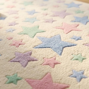 May include: A rectangular area rug with a cream-colored base featuring a repeating pattern of tufted stars in pastel shades of pink, blue, and green. The stars vary in size and are distributed across the textured surface of the soft fabric rug.