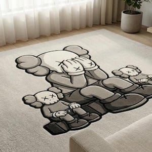 K&ouml;nnte beinhalten: Ein gro&szlig;er, rechteckiger Teppich mit einem stilisierten Cartoon-Motiv in Graut&ouml;nen. Die Hauptfigur bedeckt die Augen, umgeben von zwei kleineren Figuren. Der Teppich liegt auf einem hellen Holzboden, passend f&uuml;r ein Wohnzimmer.