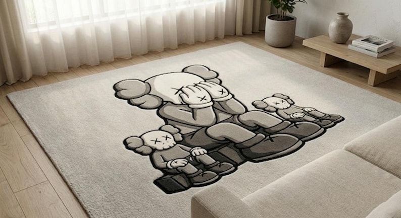 K&ouml;nnte beinhalten: Ein gro&szlig;er, rechteckiger Teppich mit einem stilisierten Cartoon-Motiv in Graut&ouml;nen. Die Hauptfigur bedeckt die Augen, umgeben von zwei kleineren Figuren. Der Teppich liegt auf einem hellen Holzboden, passend f&uuml;r ein Wohnzimmer.
