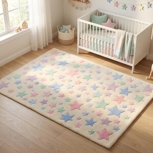 Overhead lifestyle shot of a hand tufted wool area rug with scattered pastel stars in soft pink, lavender, sky blue, and mint green on an ivory cream background, placed in a sunlit nursery room with a white crib, rocking chair, and wooden toys, showcasing a plush whimsical floor carpet perfect for baby and toddler bedrooms.