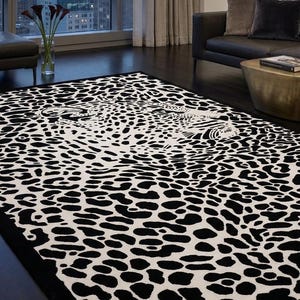 May include: A rectangular area rug featuring a high-contrast black and white leopard print pattern. The design displays a stylised feline face integrated into the spotted motif, with a solid black border framing the entire piece on the floor.