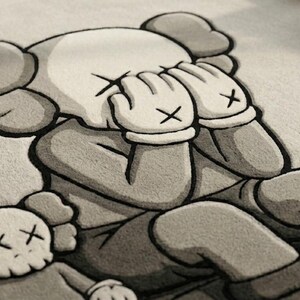 K&ouml;nnte beinhalten: Ein grau-wei&szlig;er Teppich mit einer Cartoonfigur, die sich die H&auml;nde vors Gesicht h&auml;lt. Die Figur hat gro&szlig;e Ohren und Handschuhe mit einem "X" auf jeder Hand. Zwei kleinere Versionen der Figur sind ebenfalls vorhanden.
